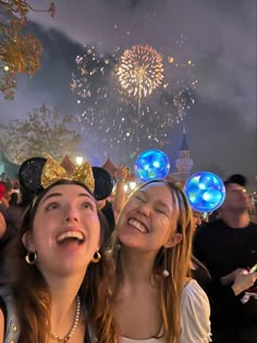 two girls wearing mickey mouse ears and glowing headbands with fireworks in the background