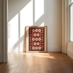 a red and white rug sitting on top of a wooden floor next to a window