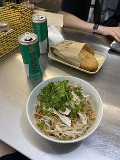 a white bowl filled with food next to a can of soda and a drink on a table