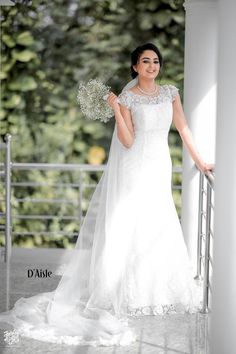 a woman in a wedding dress standing on a balcony with her arms out and flowers in her hand