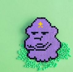 an image of a pixelated purple creature on green background with beads and sprinkles