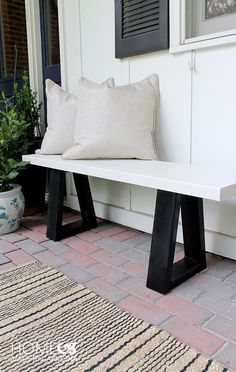 a white bench sitting on top of a wooden floor next to a rug and pillows