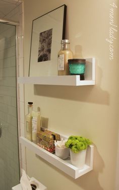 two white floating shelves in a bathroom next to a toilet and shower with green flowers on the shelf