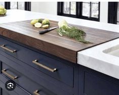 a cutting board on top of a kitchen counter next to some fruit and vegetables in front of the sink