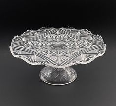 a clear glass cake plate on a black surface with an intricate design in the center