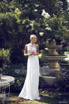 a woman in a white dress standing next to a table and fountain with flowers on it