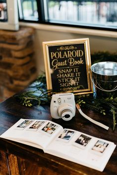 a polaroid camera sitting on top of a wooden table next to an open book