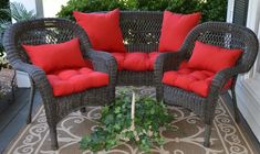 two wicker chairs sitting on top of a rug in front of a porch with red pillows