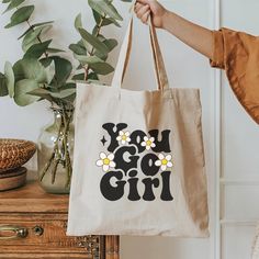 Super cute canvas inspirational tote bag. Great gift for a special friend or for yourself. Tote has two different graphics on it, one shown on the front side of the bag 'You Go Girl' and one on the back 'Be A Kind Human'. This 100% cotton bag comes in one size - 15" x 16"- perfect for everyday wear. The canvas material is durable and will last for years. The bag features 20" handles (made from the same canvas), making it easy to carry even with a week's worth of shopping. .: 100% cotton canvas .: Heavy fabric .: Sewn-in label Cute Cotton Shoulder Bag With Letter Print, Cute Canvas Bag With Letter Print For School, Cute Letter Print Canvas Bag For School, Cute School Canvas Bag With Letter Print, Cute Canvas Bag For Gifts, Trendy White Canvas Bag For Gifting, Trendy White Canvas Bag As A Gift, Trendy White Canvas Bag As Gift, Graphic Print Rectangular Canvas Bag Gift