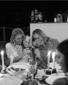 two women sitting at a table with wine glasses in front of them and candles on the table