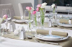 the table is set with white and pink flowers in vases, silverware, and napkins