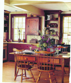 an old fashioned kitchen with wooden furniture and flowers on the dining table in front of it