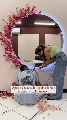 a woman standing next to a man in front of a mirror with flowers on it