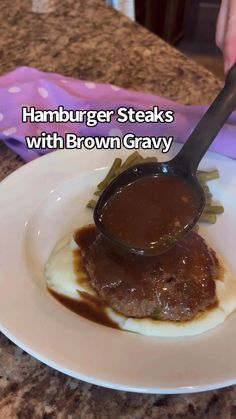 a white plate topped with meat covered in gravy next to a pink napkin