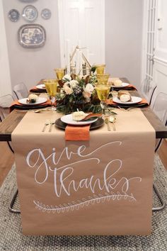 a table set for thanksgiving dinner with place settings and napkins on it, along with an orange runner