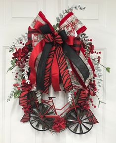 a red and black christmas wreath hanging on the front door with ribbons, bows and decorations