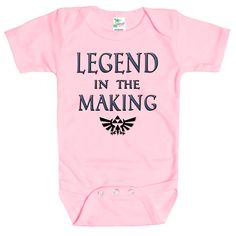 Rapunzie's adorable baby onesie, perfect for little ones who are destined to become legends! Made from 100% cotton, this short-sleeve onesie ensures utmost comfort for your precious bundle of joy. With its charming design featuring the iconic Legend of Zelda video game symbol and the captivating caption, "Legend in the Making," your baby will surely make a statement wherever they go.Crafted with love and attention to detail, this baby onesie combines style and softness to create a delightful out Pink Cotton Onesie For Gift, Short Sleeve Onesie With Funny Text For Birthday, Pink Cotton Onesie As A Gift, Pink Cotton Onesie As Gift, Casual Short Sleeve Onesie With Funny Text For Birthday, Funny Text Short Sleeve Onesie For Birthday, Pre-shrunk Short Sleeve Onesie For Playtime, Short Sleeve Onesie With Funny Text For Parenting, Funny Customizable Short Sleeve Onesie