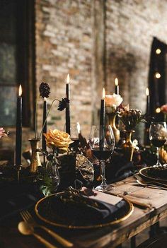 the table is set with black and gold plates, silverware, candles and flowers