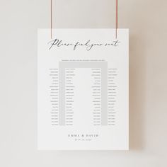 a wedding seating chart hanging from a string on a white wall next to a plant