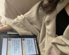 a woman sitting on a couch holding a tablet with a book in front of her