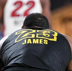 the back of a man wearing a black jersey with yellow lettering on it and his hands behind him