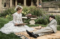 a man and woman sitting on top of a blanket in the grass next to each other