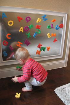 a toddler playing with magnetic letters in front of a glass door on the floor