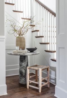 a table with a vase on it next to a stair case in a room that has white walls and wood floors