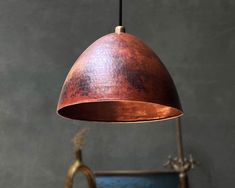 a copper colored pendant light hanging from a metal ceiling fixture over a blue bucket with a plant in it