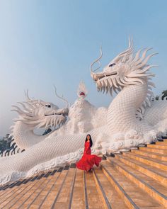 a woman in a red dress standing on steps next to two white dragon statues