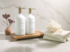 two white bottles sitting on top of a wooden tray next to towels and a vase