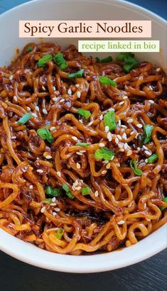 spicy garlic noodles in a white bowl with sesame seeds and green garnishes