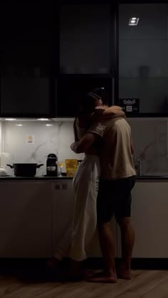 a man and woman hug in the kitchen at night, as they prepare food for dinner