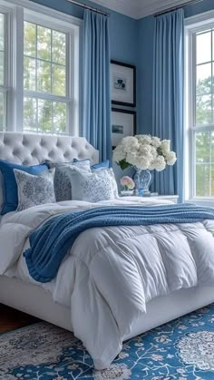 a bedroom with blue walls and white bedding, windows, and rugs on the floor