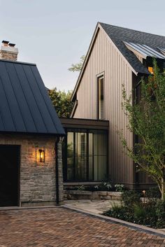 a house with a black metal roof and brick driveway