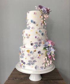 a three tiered white cake with flowers on the top and bottom, sitting on a wooden table