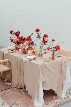 the table is set with pink flowers and plates on it, along with gold chairs