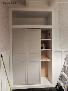 an empty closet with shelves and ladders in the corner, next to a wallpapered wall