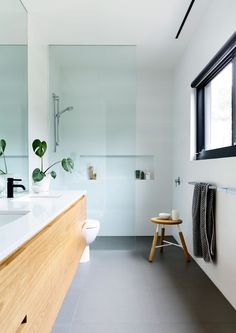 a white bathroom with a wooden stool next to the sink and mirror above the toilet