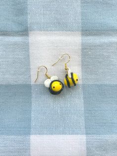 two small yellow and black beads are hanging from the ear hooks on a blue checkered fabric