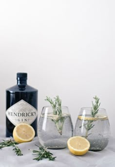 three glasses with lemons and rosemary in them next to a bottle of hendrick's gin