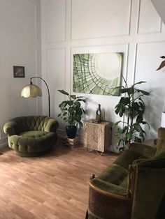 a living room with two green chairs and a painting on the wall above it's windows