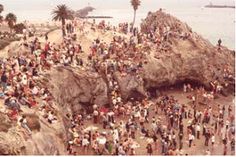 a crowd of people standing on top of a beach next to the ocean