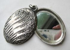 an antique silver locke with a mirror in the middle on a white surface, showing it's reflection