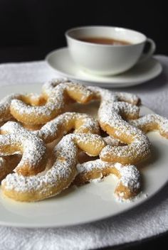 powdered sugar coated doughnuts on a plate next to a cup of coffee