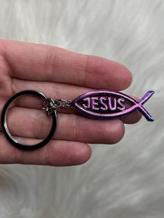 a hand holding a keychain that has a fish on it and the word jesus painted on it