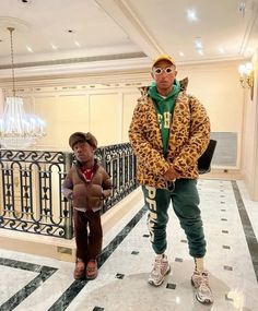 two young men standing next to each other in front of a stair case and chandelier