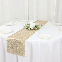 the table is set with white plates and gold linens for an elegant dinner party