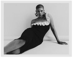 a black and white photo of a woman in a dress laying on the floor with her legs crossed