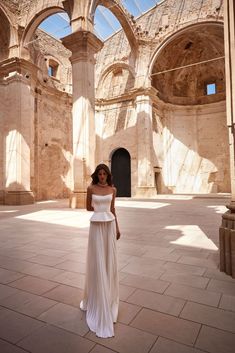 a woman in a white dress is posing for a photo inside an old building with arches